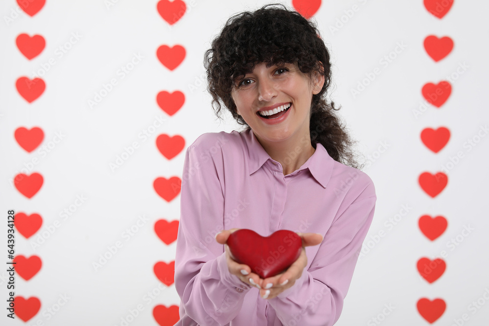 Happy young woman holding decorative red heart on decorated background Happy young woman holding decorative red heart on decorated background