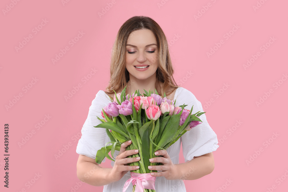 Happy young woman with bouquet of beautiful tulips on pink background