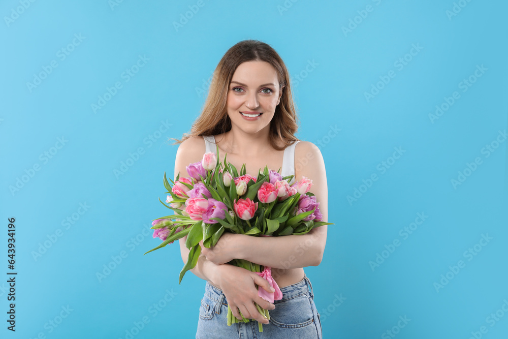 Happy young woman with bouquet of beautiful tulips on light blue background