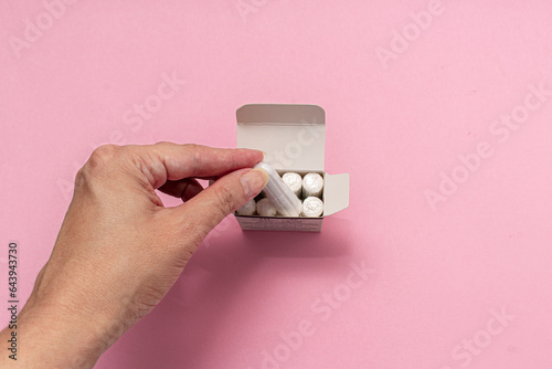 The concept of feminine hygiene, tampons on a pink background. Woman's hand holding a white tampon