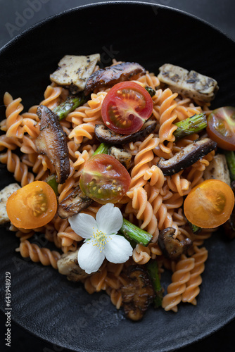 Fusilli pasta with mushrooms, asparagus and cherry tomatoes on a modern design plate with dark background