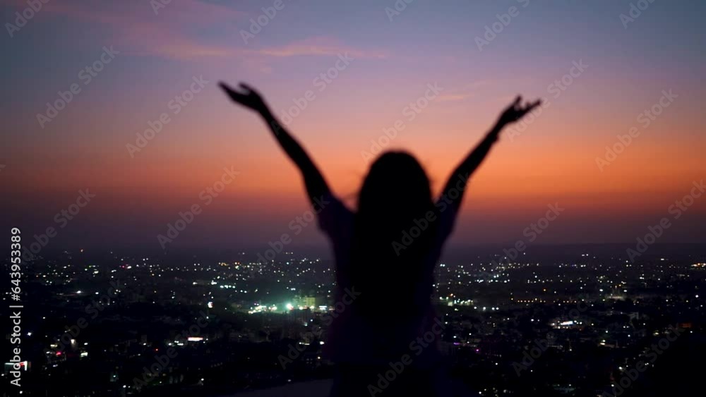 Silhouette of defocused Indian girl raises her hands up in front of city during night. Travel concept. Concept of welcoming, relaxing and enjoying. Silhouette of defocused Indian girl raises her hands up in front of city during night. Travel concept. Concept of welcoming, relaxing and enjoying.