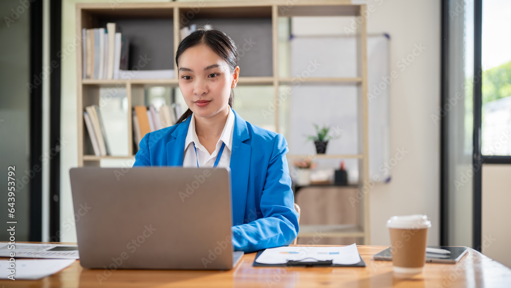A confident Asian businesswoman is working on her laptop at her desk in the office. A confident Asian businesswoman is working on her laptop at her desk in the office.