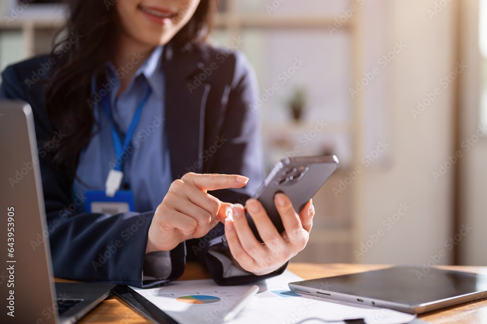 A businesswoman is checking SMS or sending messages on her smartphone while sitting at her desk A businesswoman is checking SMS or sending messages on her smartphone while sitting at her desk