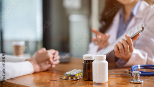 Two bottles of medicine, pills, and a stethoscope on a table in a doctor's examination room.