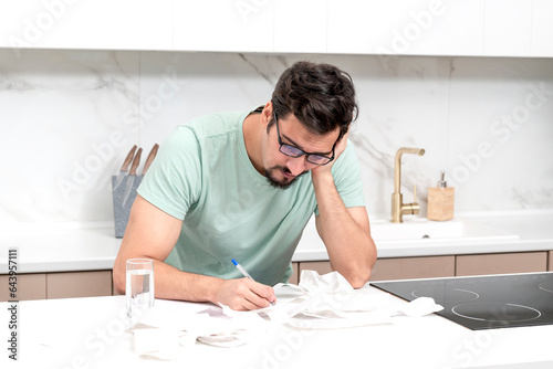 Close up of unhappy man sitting at the table, stressed and confused by calculate expense from invoice or bills, have no money to pay mortgage or loan. High prices and spending money concept