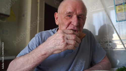 Elderly senior man eating soup with bread and green onion at home in the kitchen. Happy retirement, simple whole food.