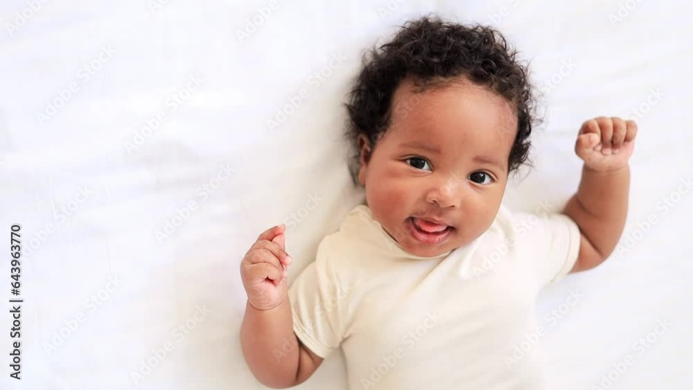 little african American baby girl in a white bodysuit on a cotton bed at home, six-month-old smiling joyful black baby little african American baby girl in a white bodysuit on a cotton bed at home, six-month-old smiling joyful black baby