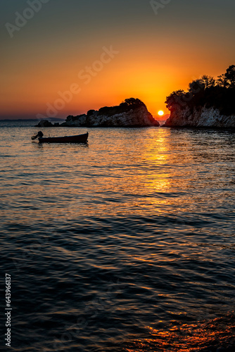 Sunset over the sea. The sun is setting between two rocks in the horizon  with a small motor boat anchored near by 