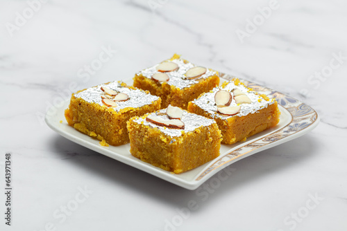 Close-up of an Indian Sweet "Moong daal Barfi" decorated with silver leaf dry fruits. Isolated on a Marble background. Front view.