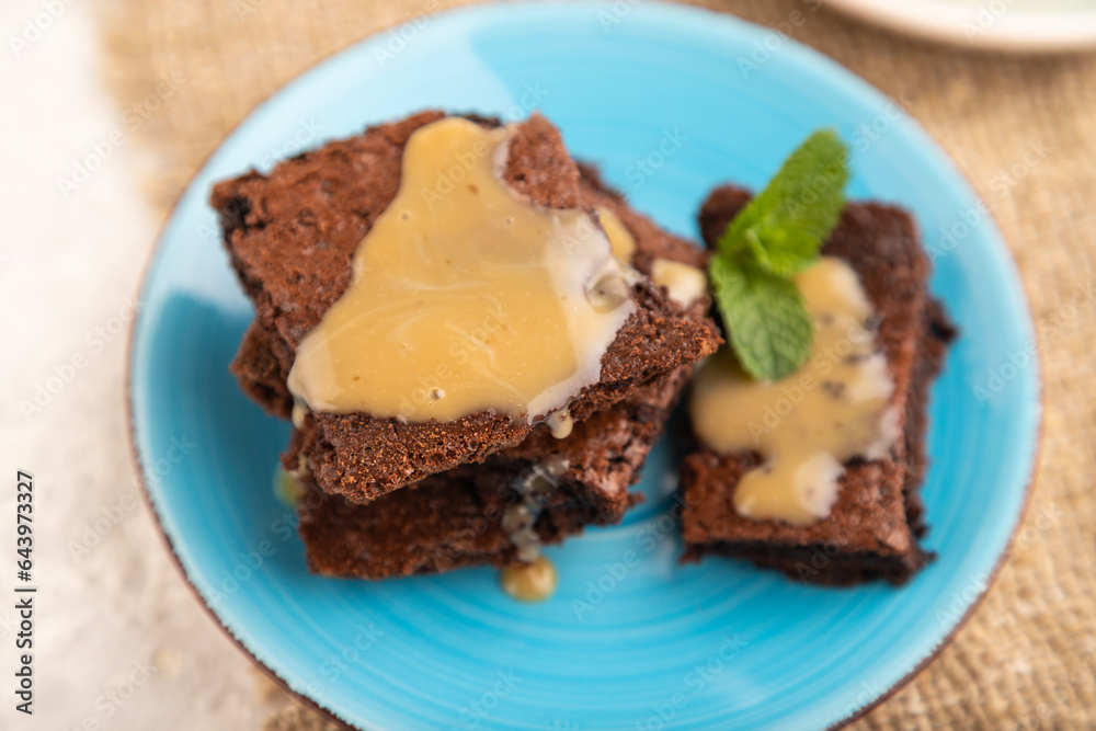 Chocolate brownie with caramel sauce with a cup of coffee on gray concrete, side view, selective focus. Chocolate brownie with caramel sauce with a cup of coffee on gray concrete, side view, selective focus.