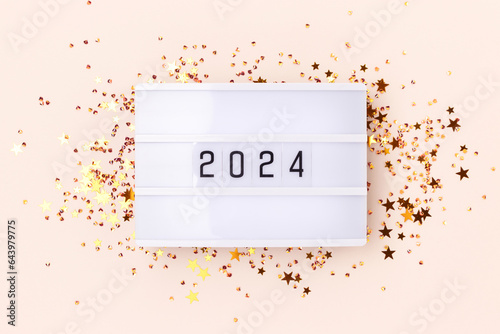 Lightbox with 2024 numbers and gold colored stars confetti on a beige background. New Year concept.