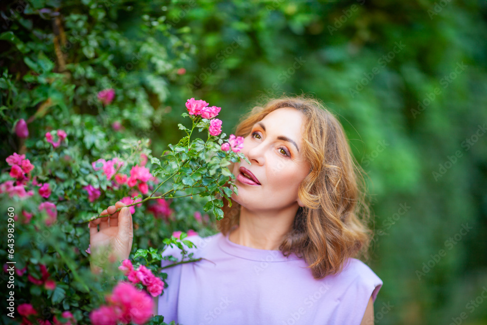 Beautiful successful middle aged woman smelling bloom roses and enjoying in garden outdoors. Beautiful successful middle aged woman smelling bloom roses and enjoying in garden outdoors.