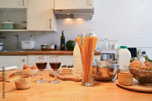 Two glasses of red wine, pastry ingredients and utensils on wooden kitchen tabletop. Copy space for your text