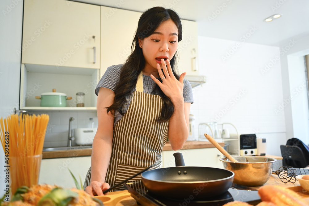 Cheerful asian housewife with spatula in hand, preparing breakfast in kitchen. People, food and domestic life concept