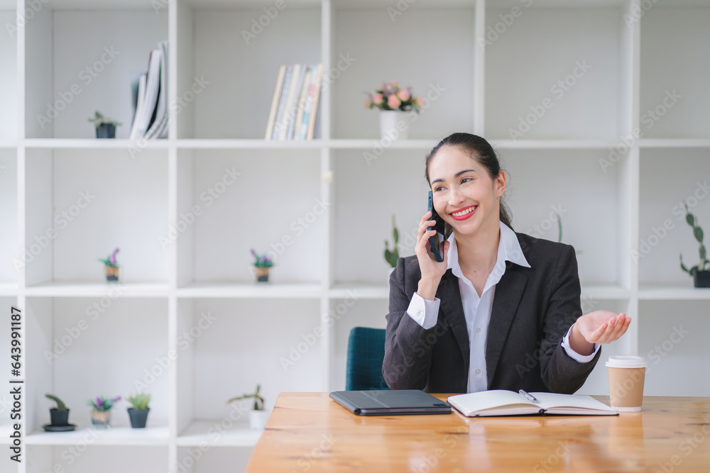 Young adult Asian businesswoman, secretary, sales manager, business consultant, engaging in a phone conversation with a client at the office. Young adult Asian businesswoman, secretary, sales manager, business consultant, engaging in a phone conversation with a client at the office.