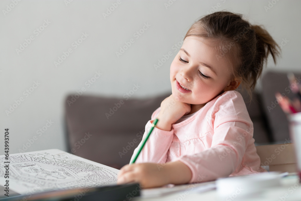 Cute smiling little girl write homework at desk at home. Happy preschooler writing with left hand indoors. Children education concept. Cute smiling little girl write homework at desk at home. Happy preschooler writing with left hand indoors. Children education concept.