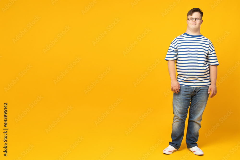 Naklejka premium Smiling young man with down syndrome in glasses posing on orange background, place for text