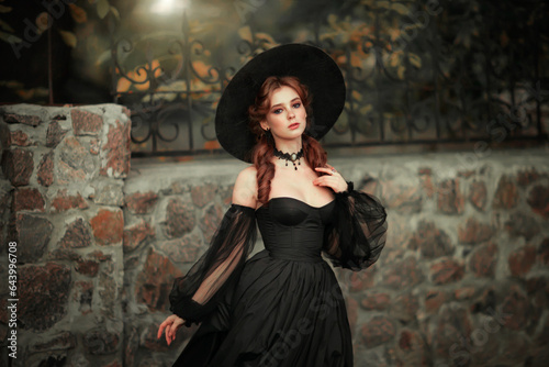 Portrait of magnificent Fashion gothic girl  .Fantasy art work.Amazing red haired model in black dress and hat looking at camera and posing.Fairytale about young princess 