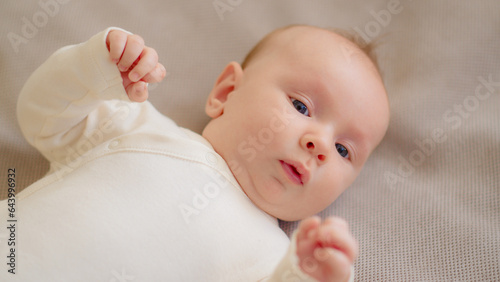 Sweet newborn boy lies on the sofa. Beautiful infant boy with blue eyes.  Cute two-month-old baby in white clothes. High angle view of a chubby male kid.  Closeup portrait of calm baby.