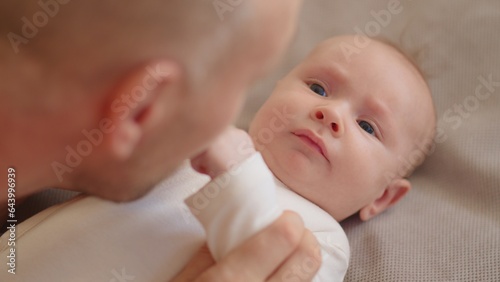 Dad playing with a newborn baby. Cute baby is trying to pronounce sounds while looking at his dad. Face of an active Caucasian baby looking at a parent. Father is playing with his baby.