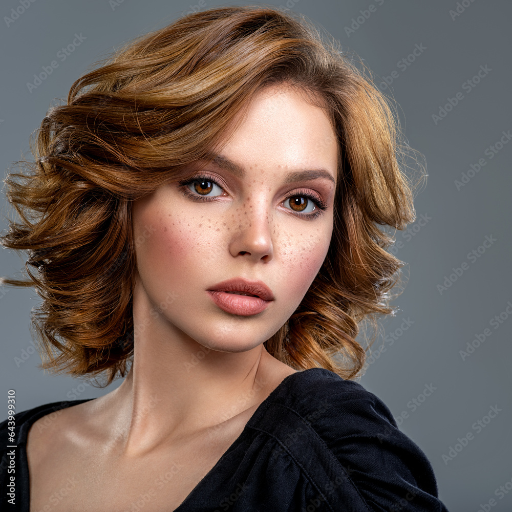 Naklejka premium Beautiful brown haired with stylish short hairstyle. Woman with a curly hair. Beautiful young woman with freckles on face. Closeup portrait of an attractive girl with a brown makeup.