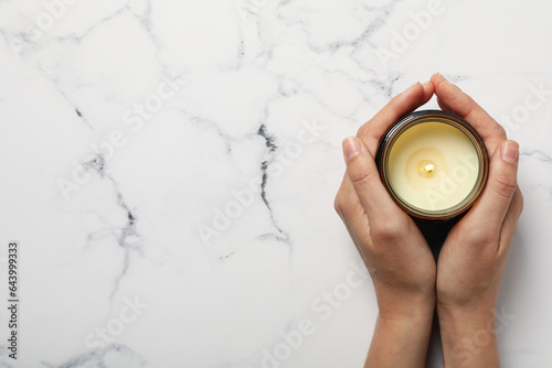 Candle in female hands on marble background, space for text