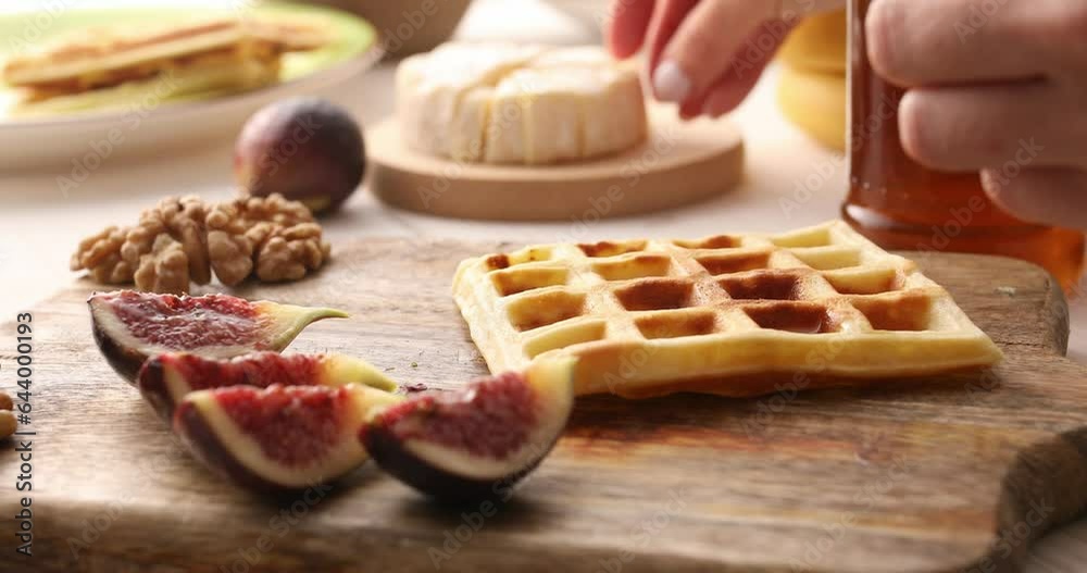 Belgian waffle is topped with brie cheese and figs. Preparing a snack or appetizer. Tasty food. Close-up. Belgian waffle is topped with brie cheese and figs. Preparing a snack or appetizer. Tasty food. Close-up.