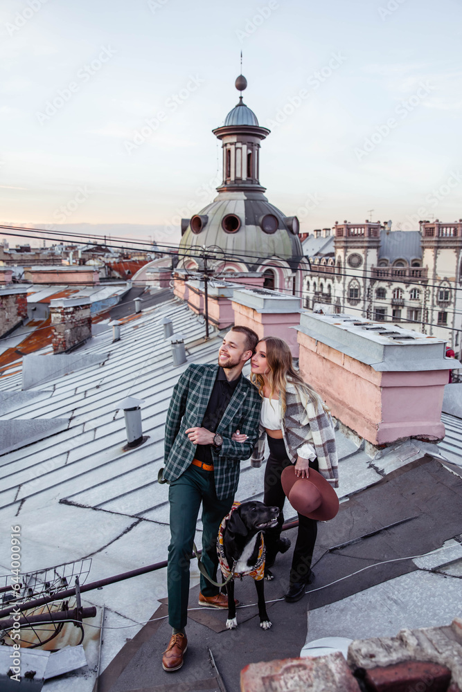 Beautiful couple in love with black dog on the roof at sunset in summer