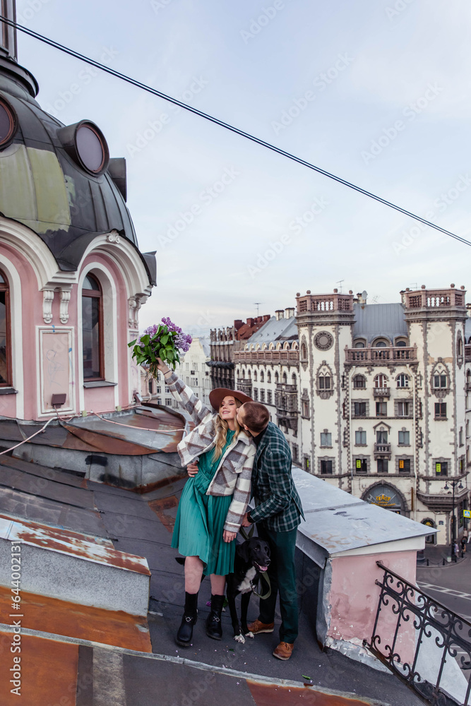 Naklejka premium Beautiful couple in love with black dog on the roof at sunset in summer