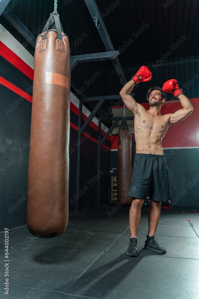 Handsome Middle Eastern man with a muscular body physique showing how to throws powerful punches at a punching bag, displaying his boxing prowess in a boxing gym