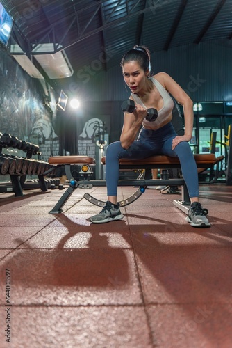 Determined young Asian woman strengthens her arm with single-arm dumbbell rows on the bench press, showing her dedication to building muscle at the gym