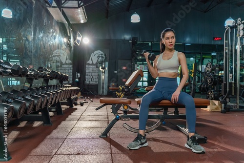 Determined young Asian woman strengthens her arm with single-arm dumbbell rows on the bench press, showing her dedication to building muscle at the gym