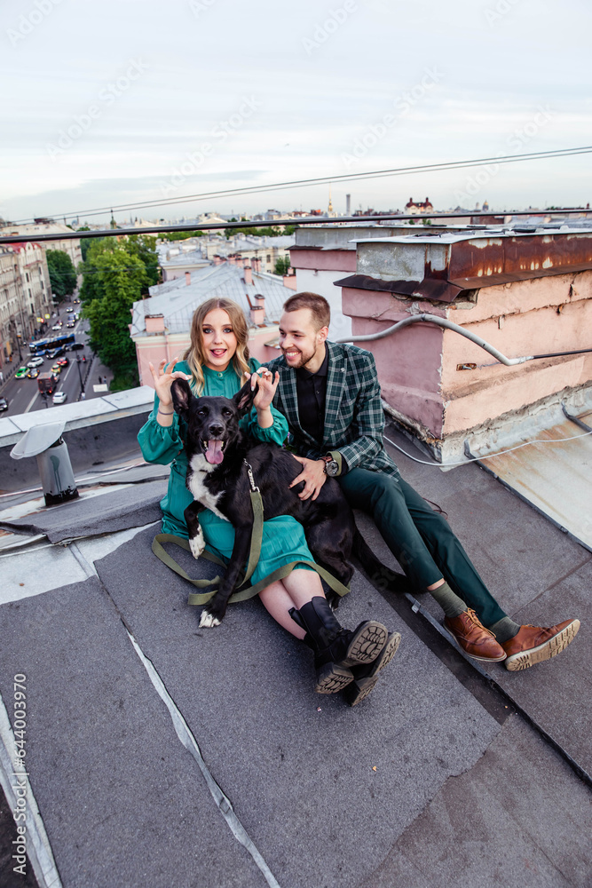 Obraz premium Beautiful couple in love with black dog on the roof at sunset in summer