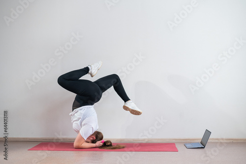 A chubby young woman watches an online yoga lesson on a laptop. Distance sports training. Forearm stand