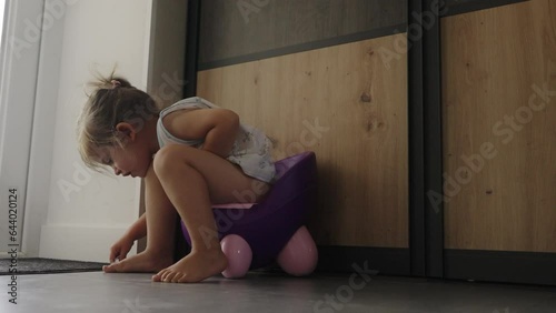 Infant child baby girl toddler sitting on potty, playing with toys in living room, indoors. Healthy lifestyle. Playing child. Baby hygiene. Domestic lifestyle.