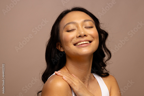 Happy asian woman with dark hair  with hand on shoulder and eyes closed