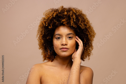 Biracial woman with dark curly hair touching face with hand