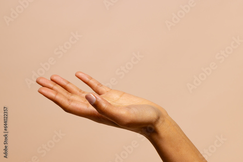 Outstretched hand of biracial woman on pink beige background with copy space