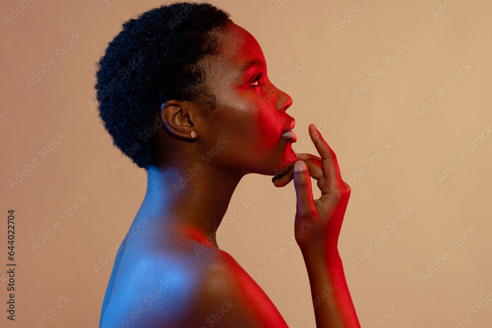 Obraz premium African american woman with short hair and white lipstick touching chin in blue and red light