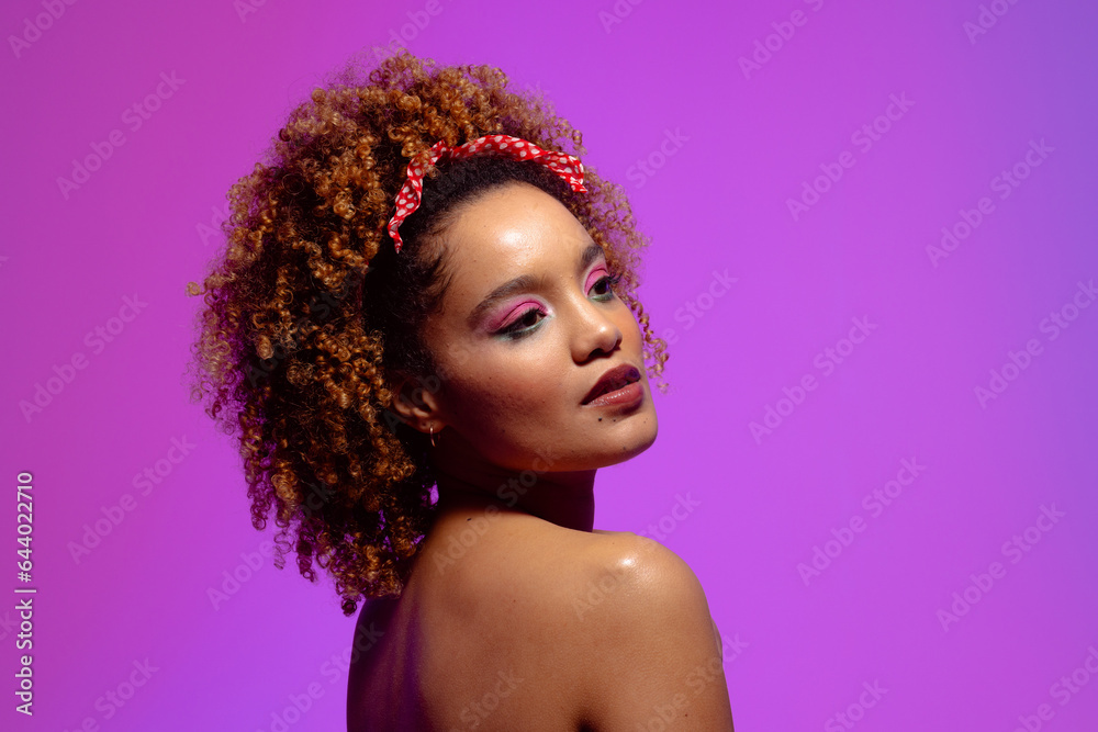 Biracial woman with curly hair, pink eye shadow and lipstick on purple background, copy space Biracial woman with curly hair, pink eye shadow and lipstick on purple background, copy space