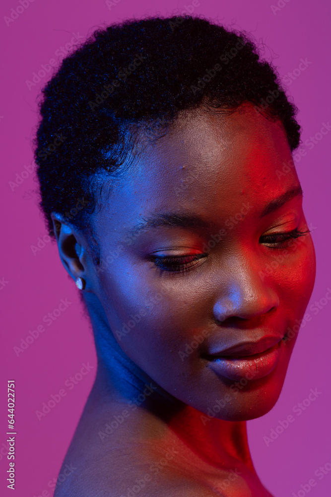 African american woman with short hair looking down in blue and red light on purple background