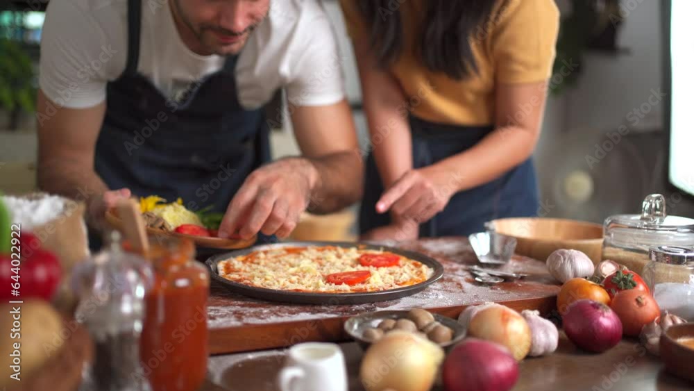 Happy lovely couple enjoy making a home made Italian pizza together at home, man adding a pizza ingredients and sauce over the pizza. Happy lovely couple enjoy making a home made Italian pizza together at home, man adding a pizza ingredients and sauce over the pizza.