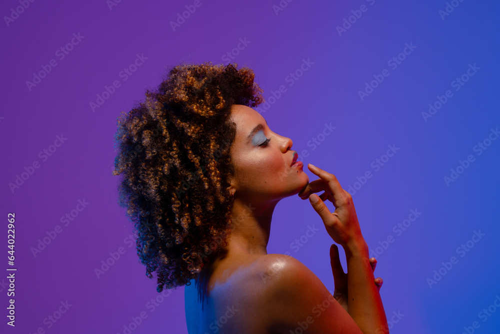Biracial woman with curly hair and blue eye shadow touching chin with eyes closed Biracial woman with curly hair and blue eye shadow touching chin with eyes closed