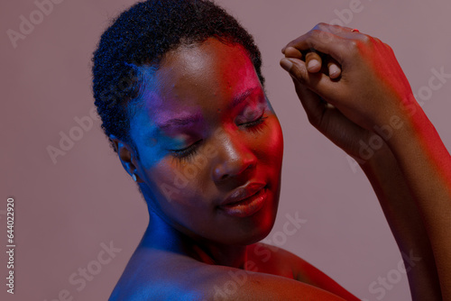 African american woman with short hair and colourful make up touching hands with eyes closed
