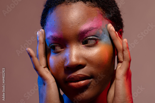 African american woman with short hair and colourful make up, looking away and touching temples