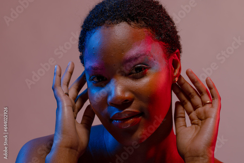 African american woman with short hair and colourful make up with hands touching ears