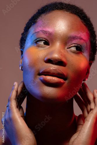 African american woman with short hair and colourful make up, looking away and touching neck