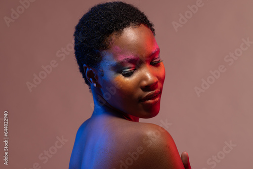 African american woman with short hair and colourful make up, looking down at shoulder