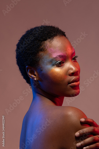 African american woman with short hair and colourful make up, looking away and holding shoulder